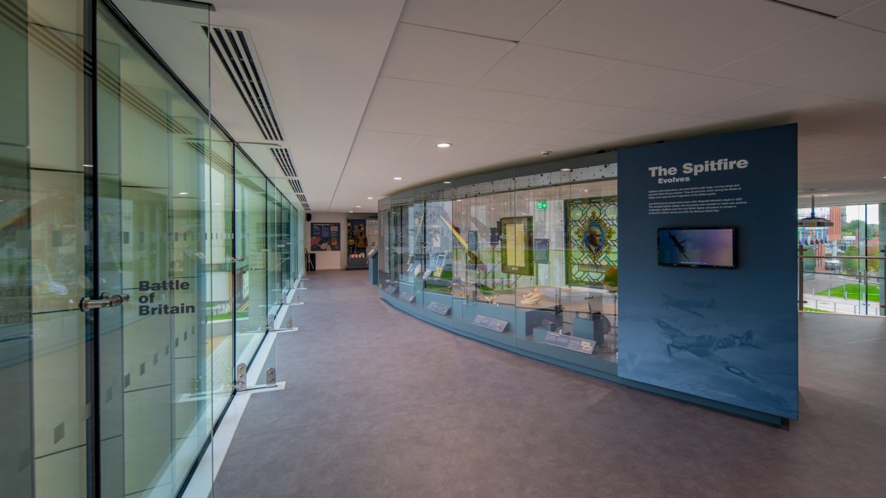 Interior of museum with glass display cases and a long wall of windows