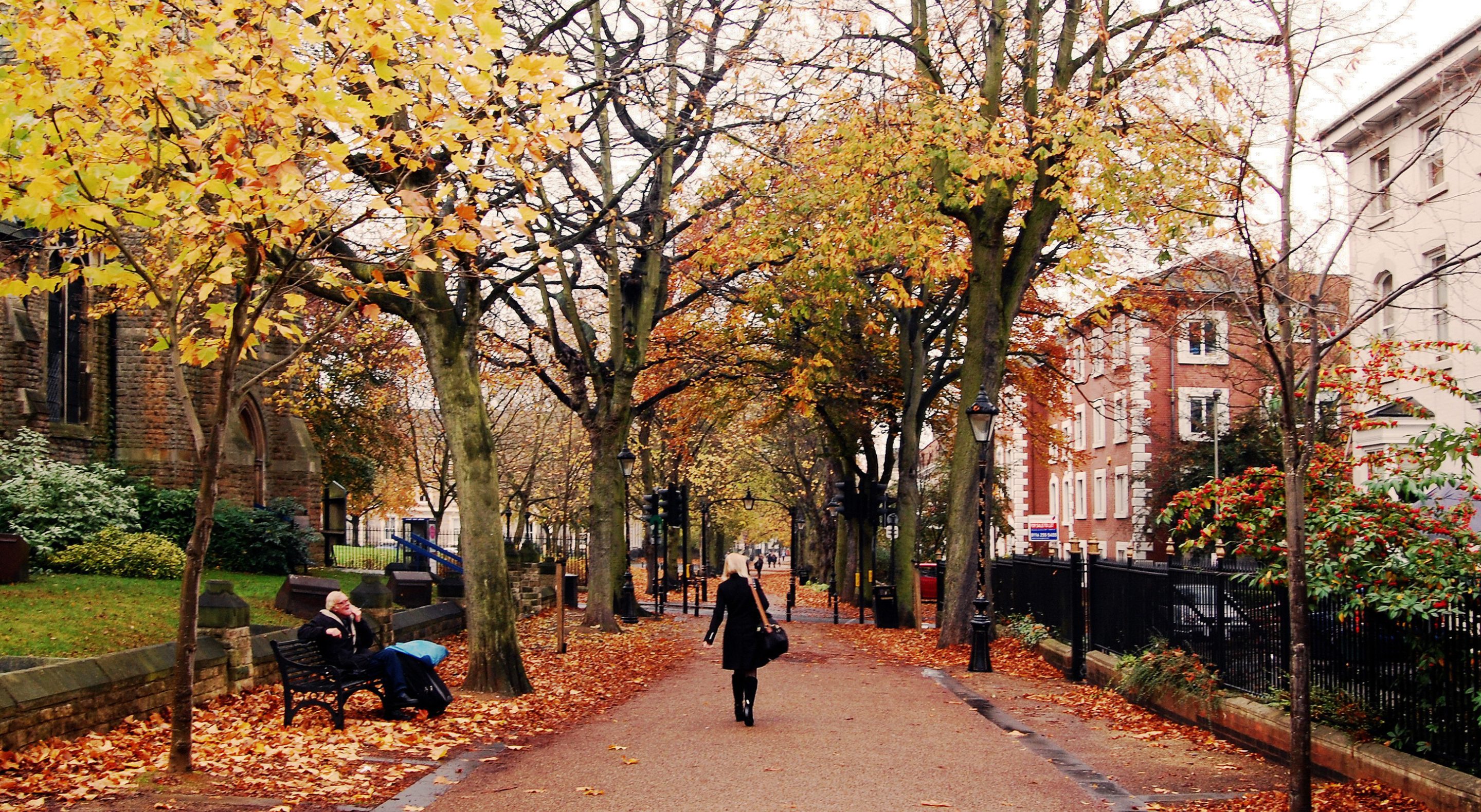 A woman walks through a leafy city path in autumn