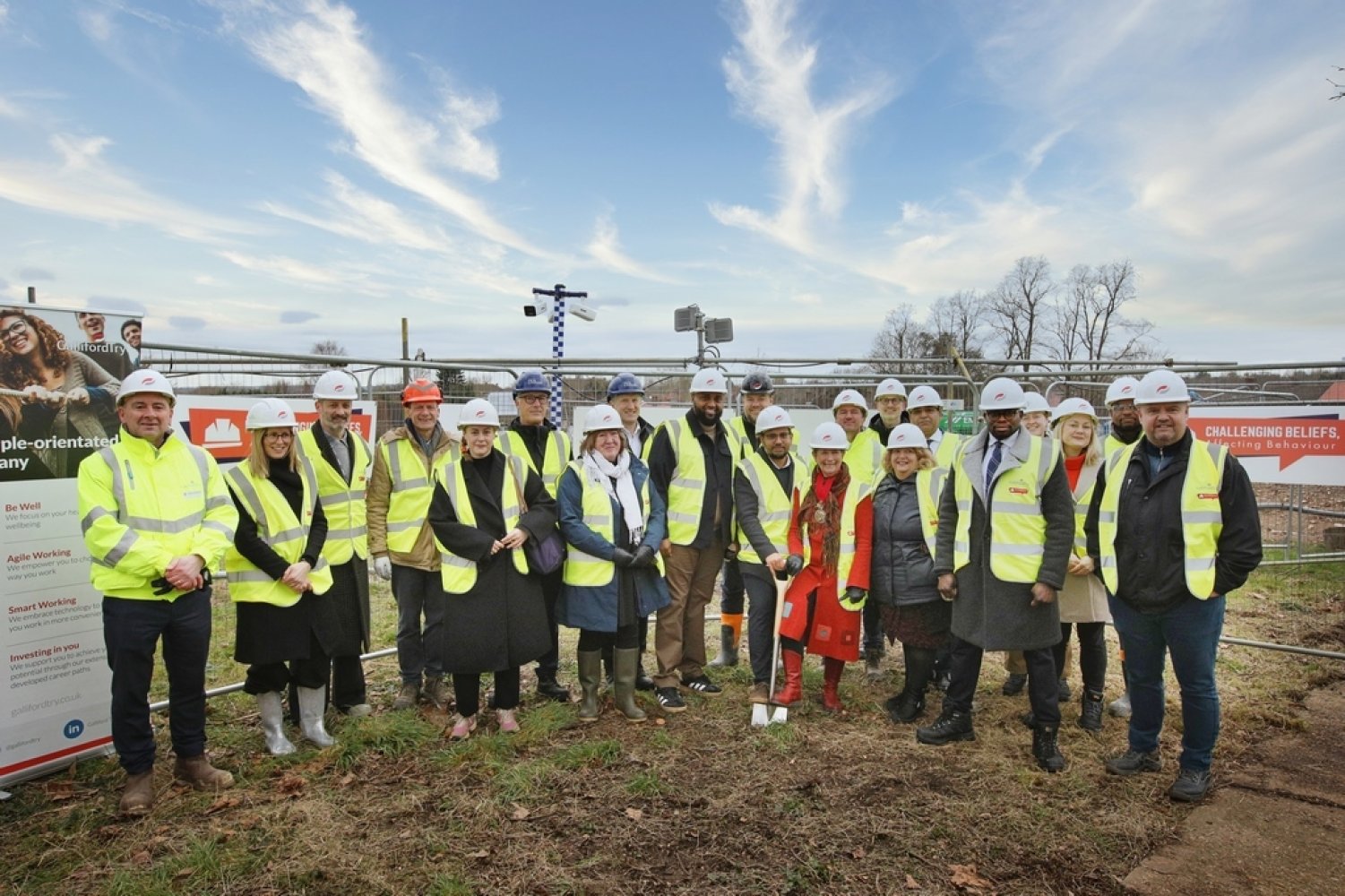 Group of people stood on the ground smiling, wearing hardhats and high vis vests