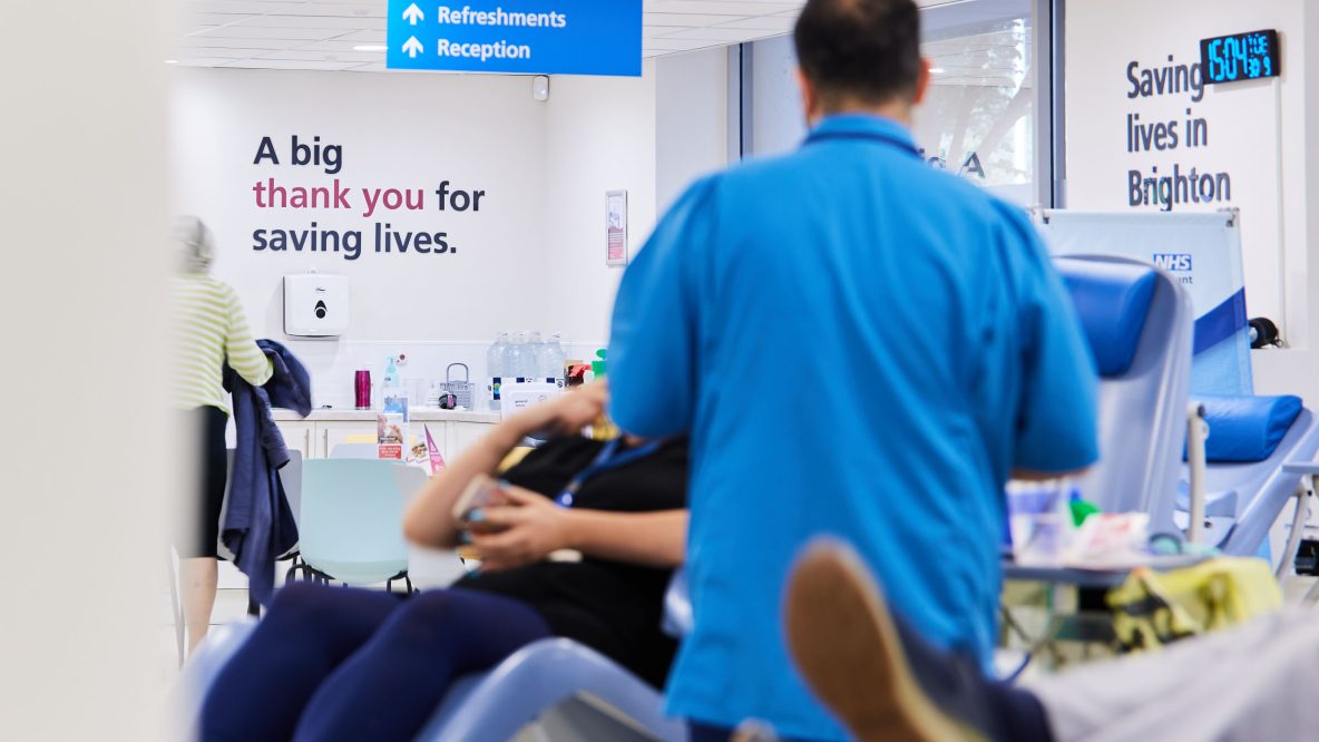 Back of NHS staff standing next to seated blood donor centre