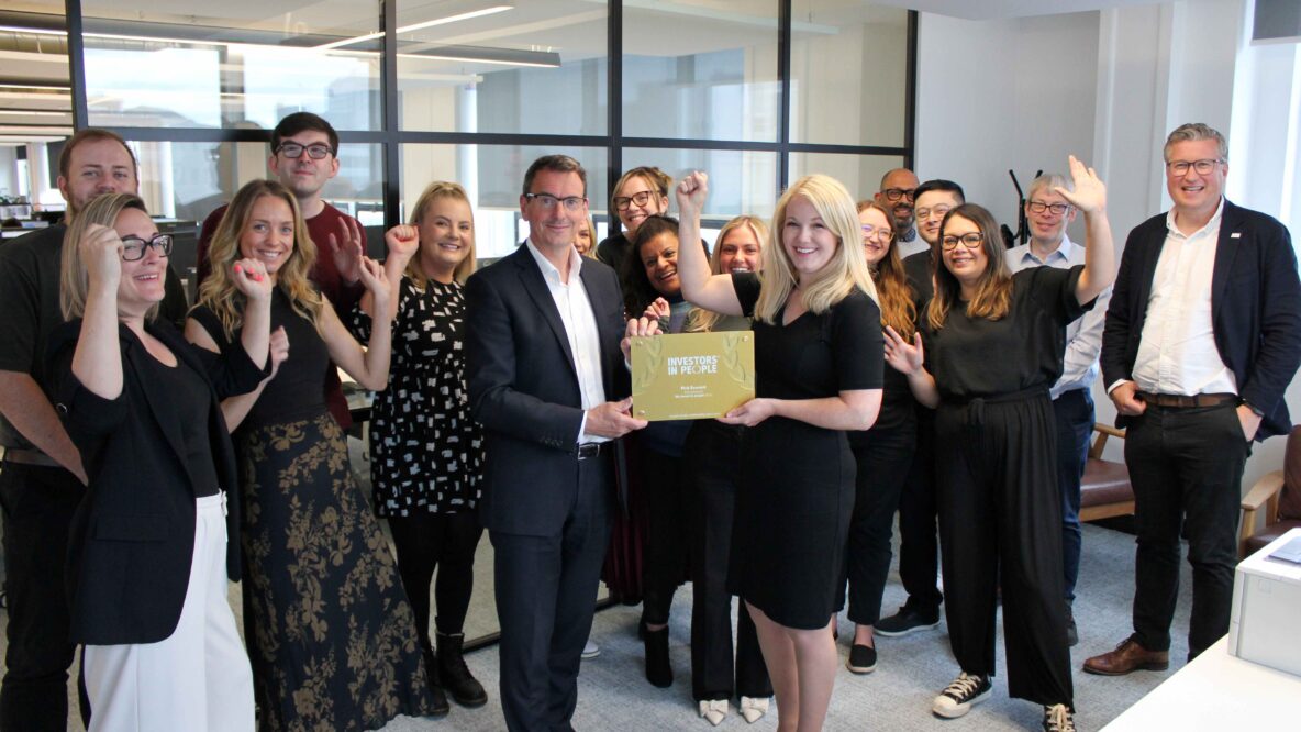 A cheerful group of people poses for a picture, holding a the investors in people gold plaque.