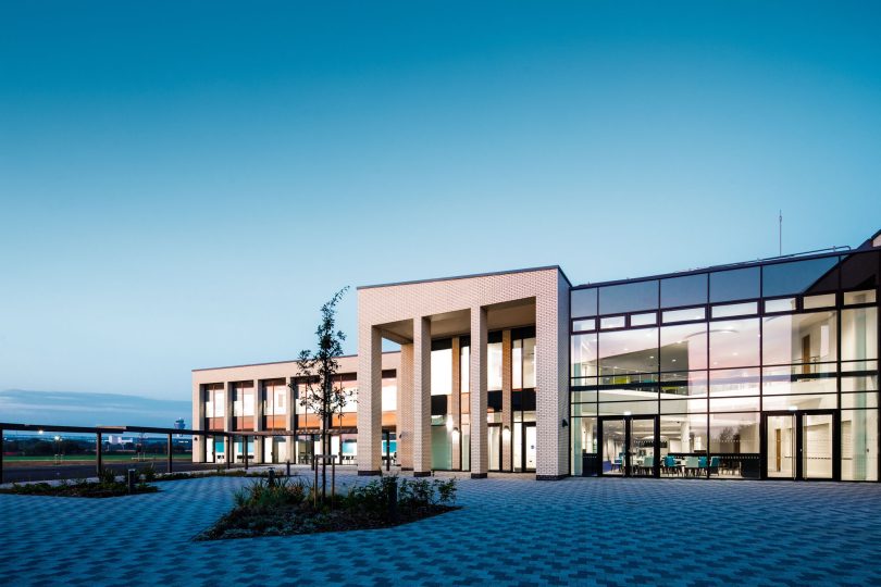 A photo of the outside of the school with blue skies and clean gardens