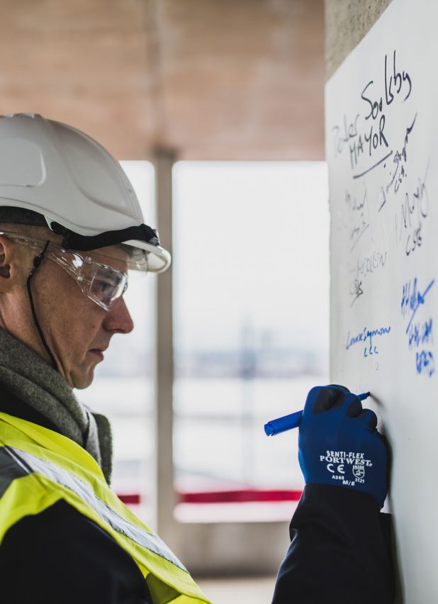 Person in hard hat writing on a white board on a building site