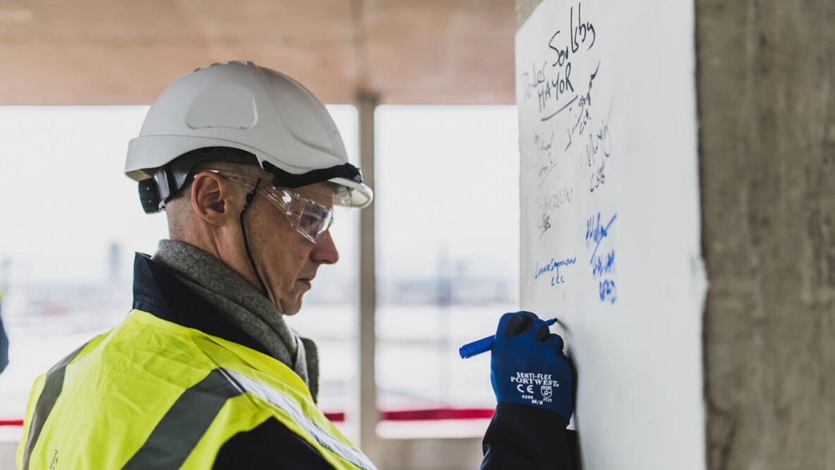 Person in hard hat writing on a white board on a building site