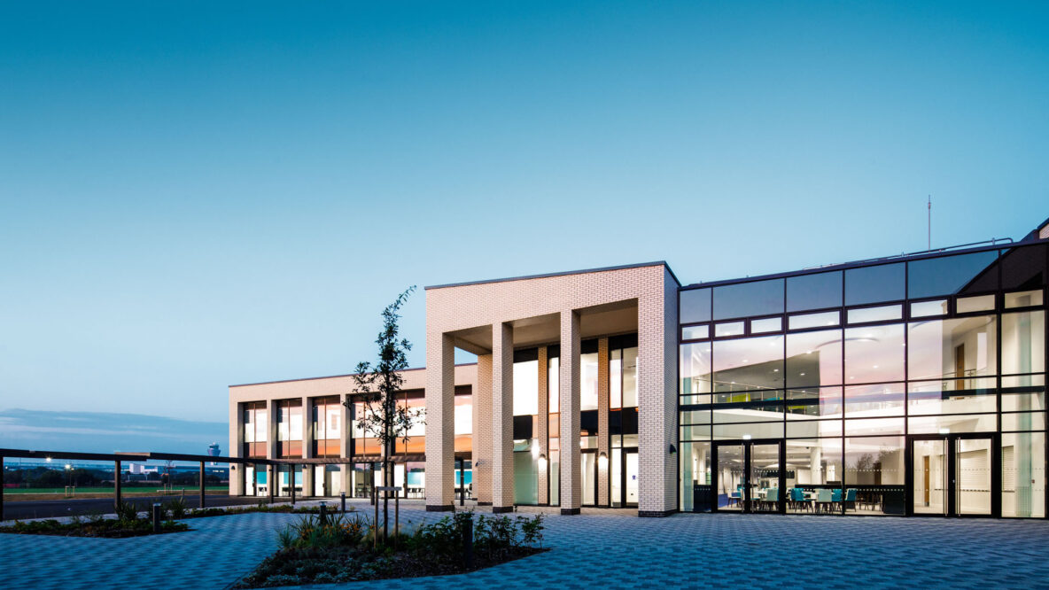 A photo of the outside of the school with blue skies and clean gardens