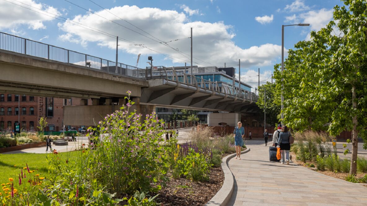 A picture of a lady walking through a park under a tram bridge