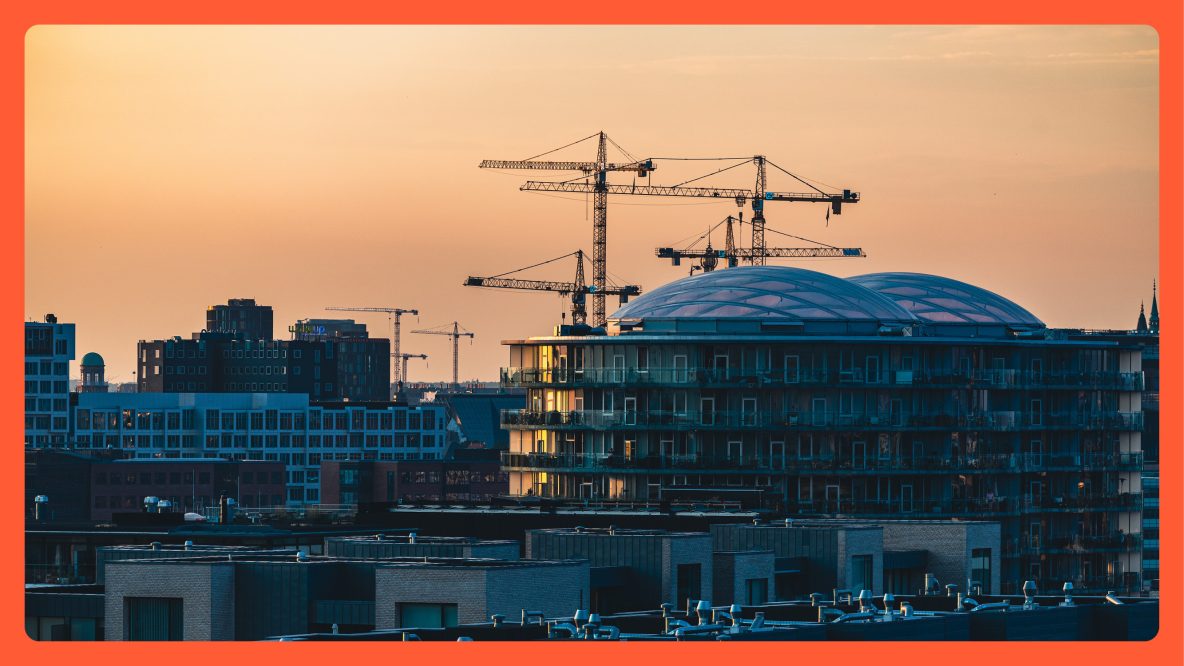 A cityscape at sunset with several construction cranes and a modern glass-domed building in the foreground, bordered by a thick orange frame.