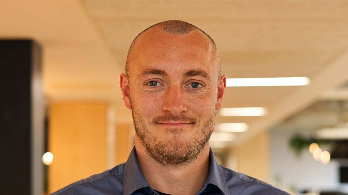 Lewis smiling at the camera in a modern office wearing a blue shirt
