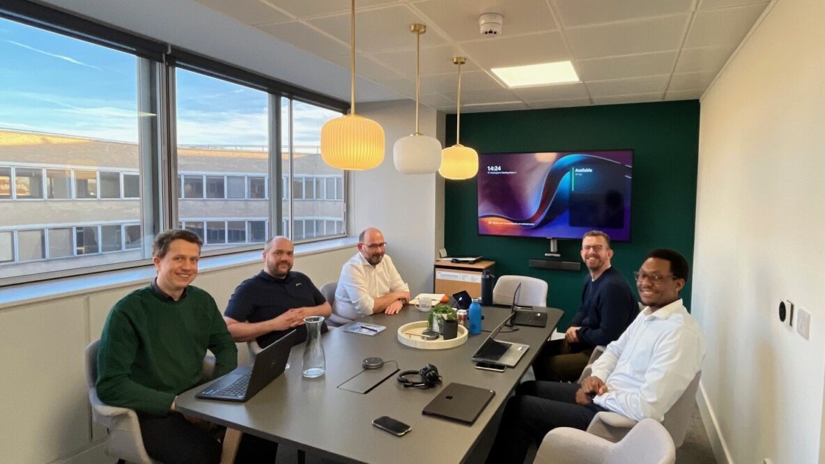 Group of five people smiling around a conference table with a screen.