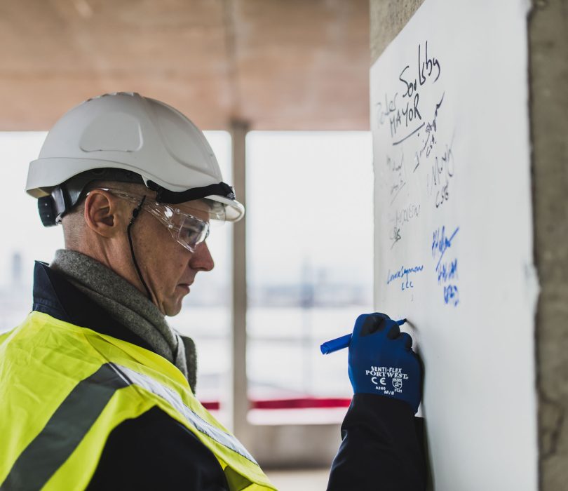 Person in hard hat writing on a white board on a building site