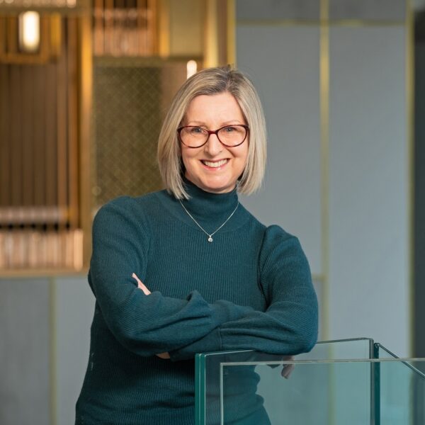 Gillian leaning on a glass handrail at the top of a staircase smiling